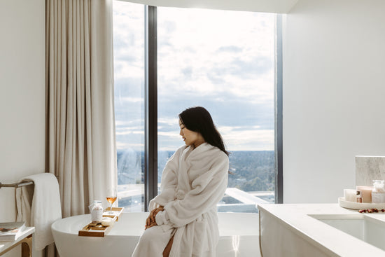 Woman in white bath robe sat on edge of bath with bamboo caddy on top of bath