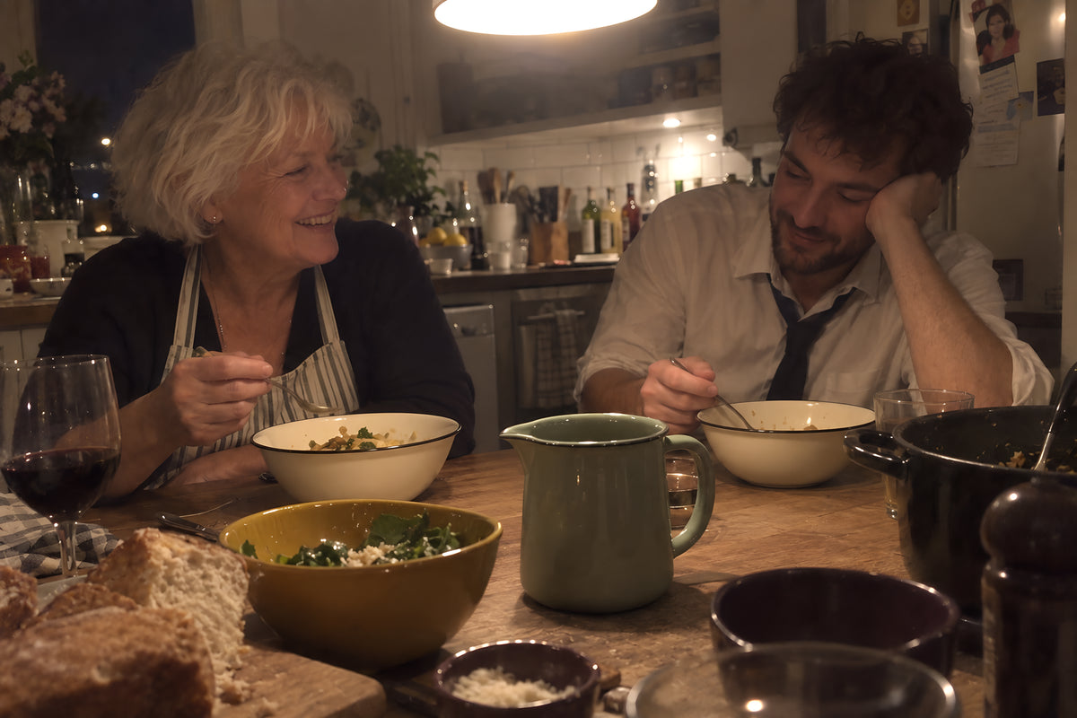 Two people eating late at a kitchen table out of cream KILN bowls, still in work clothes, one with their head propped on a hand.