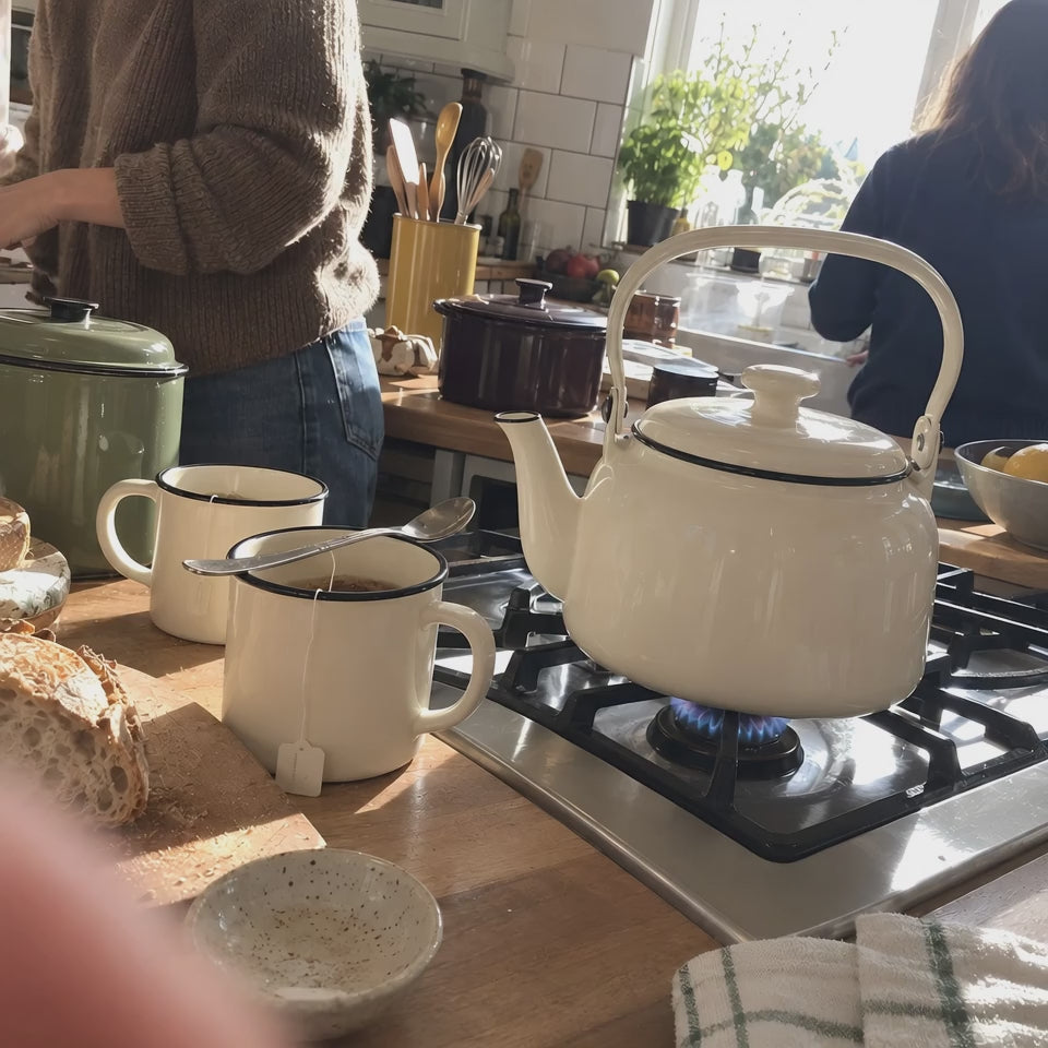 The cream KILN Kettle steaming on a gas stove beside two KILN Mugs