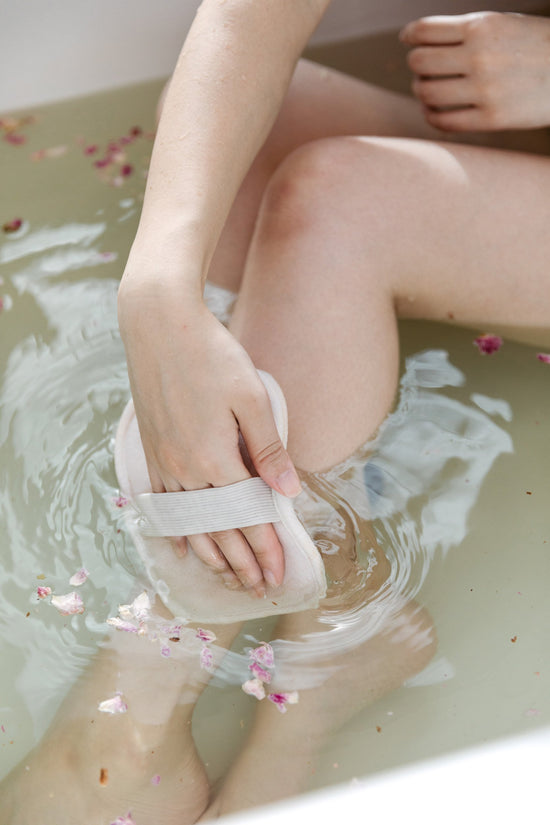 Woman in bath using bathing mitt on legs