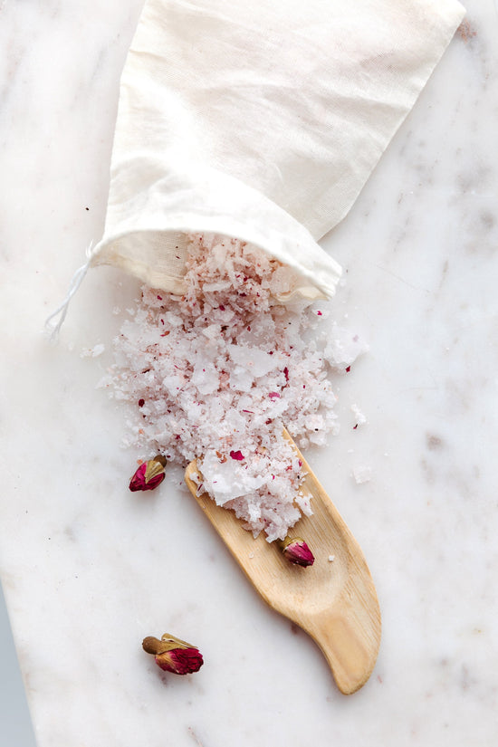 Cotton muslin bag with pink bath salts spilling out on marble counter